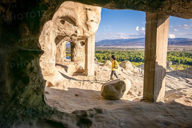 Female tourist walks around Uplistsikhe cave city exploring architectural structures. Georgia