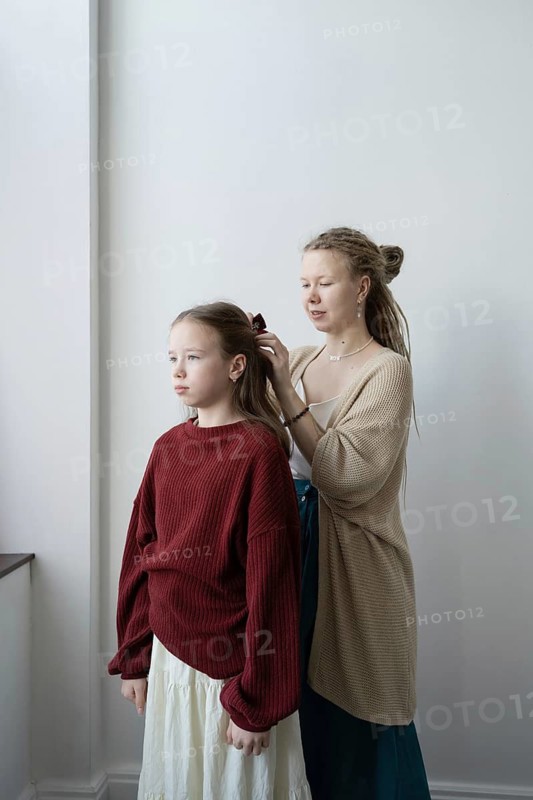 A mother lovingly styles her daughter's hair by a window in a peaceful room The scene captures the bond and tenderness in a moment of shared intimacy and care