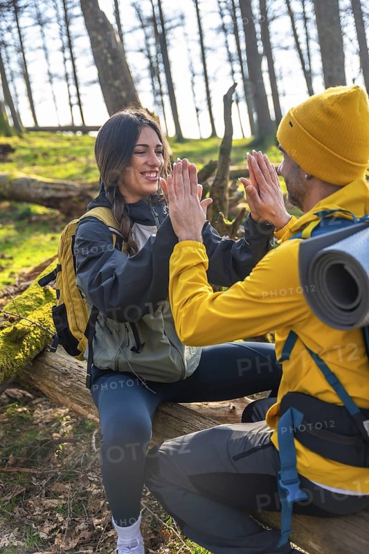 Hikers are sitting on a fallen tree trunk and giving a high five, celebrating their successful hike in the forest