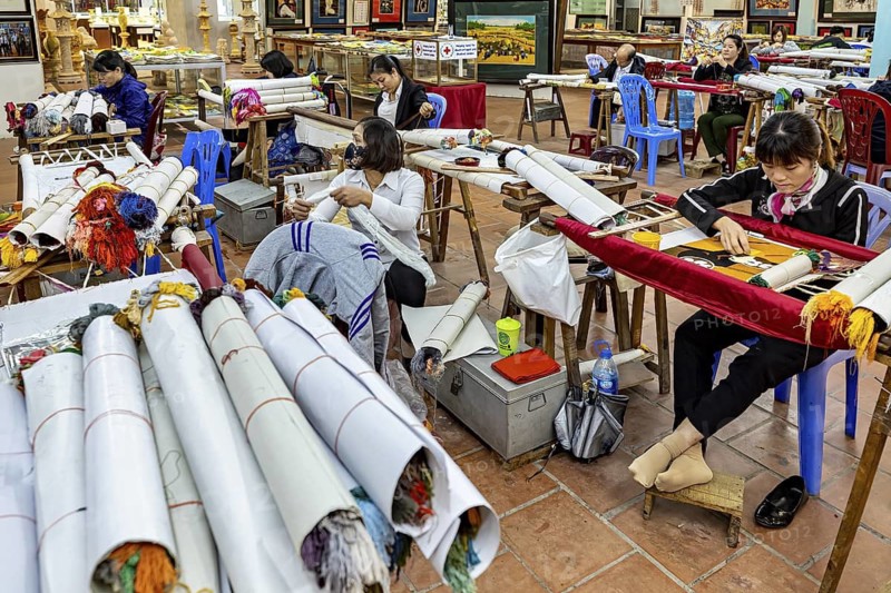 Women work in a room on traditional embroidery with colourful yarns and fabric rolls, painters and art workshop on the edge of Halong Bay in Vietnam