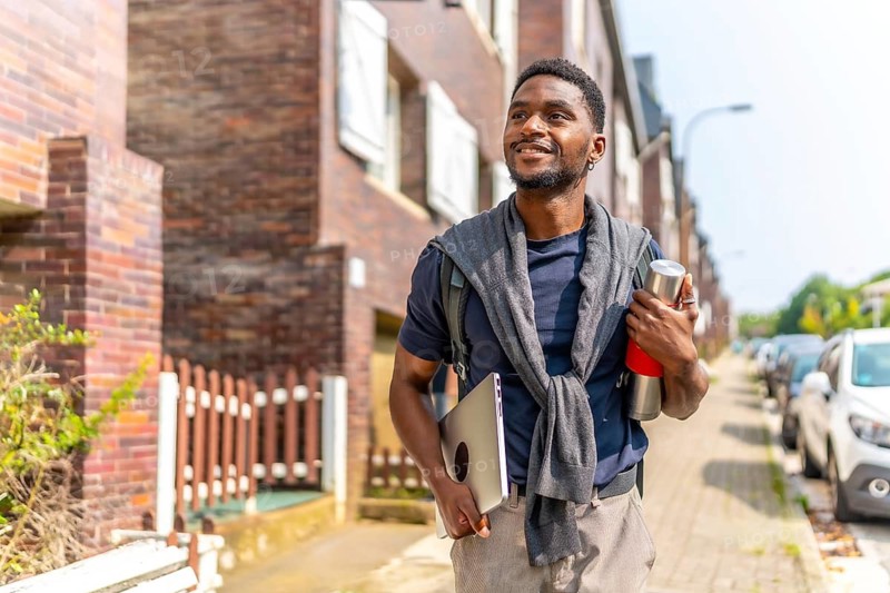 Happy african man carrying laptop and coffee thermos in the city on the way to work