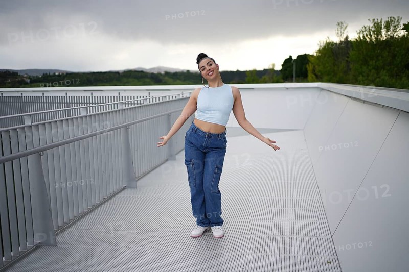 A woman in blue jeans and a blue top is standing on a white surface. She is smiling and she is enjoying herself
