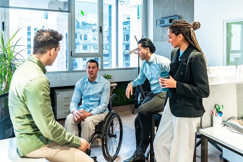Businesspeople having a conversation with a disabled colleague in a wheelchair during a meeting in a modern office
