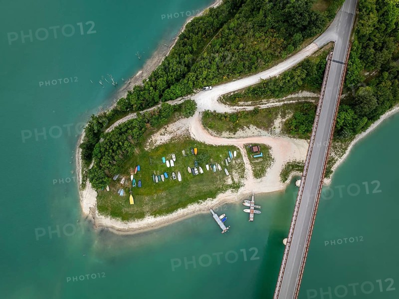 Aerial view of a serene peninsula with docked boats, lush greenery, and a bridge crossing over Castreccioni Lake, Italy. Idyllic landscape and peaceful nature