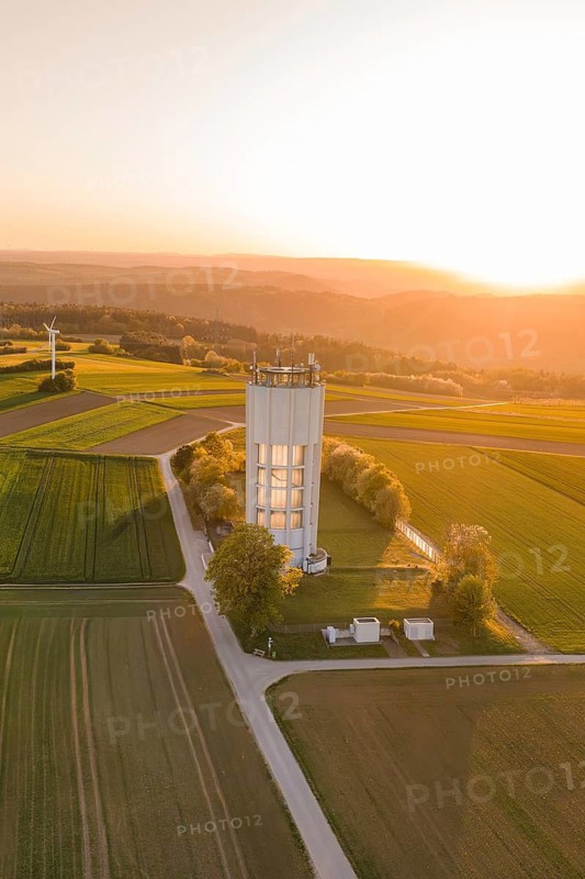 Rural landscape at sunset with water tower surrounded by green fields and a quiet, peaceful ambiance, Jettingen, Germany