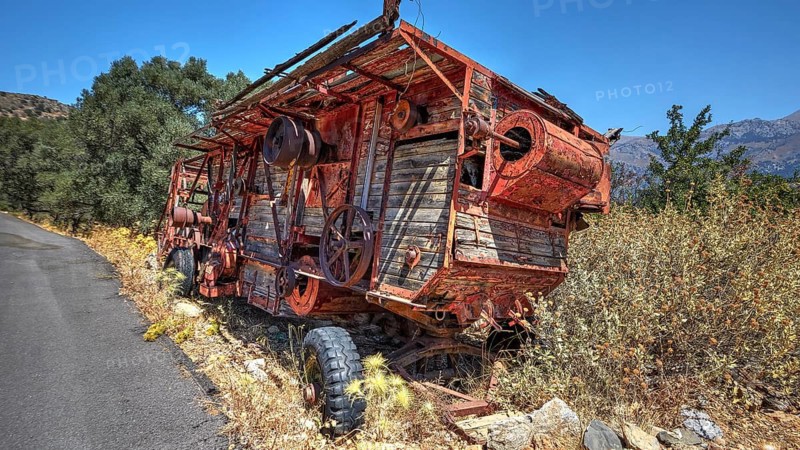 Abandoned, rusty machine next to a road with lush vegetation and mountain views in the background, Amari Basin, Amari, Central Crete, Greek Islands, Greece