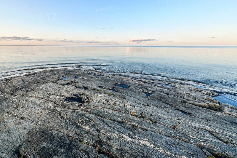 Far-reaching view of the quiet lake Vänern with gently sloping granite rocks archipelago under calm sky in the evening, Värmlands län, Sweden