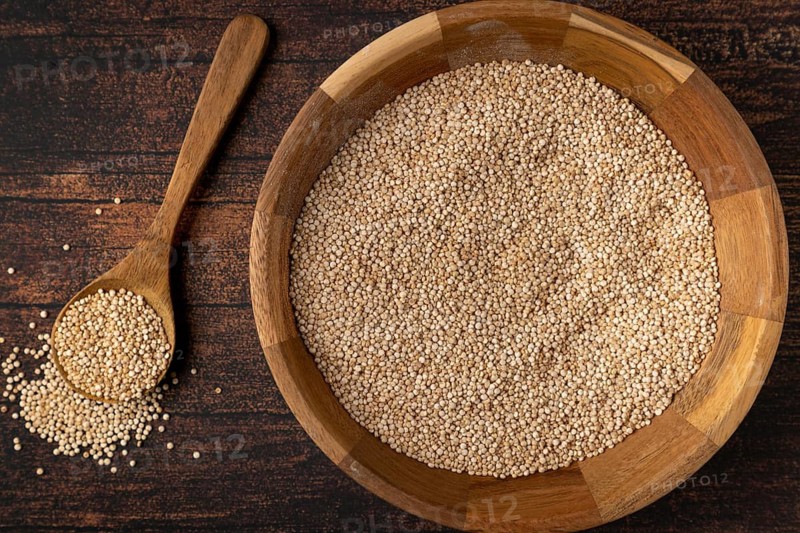 Quinoa in a wooden bowl with a spoon next to it on a dark wooden table