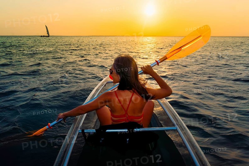 Silhouetted pretty sporty fit woman paddles clear kayak during vibrant Zanzibar sunset. Back view capturing peaceful golden hour on the Indian Ocean during a tropical tour with evening breeze
