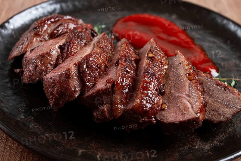 Roast duck breast, sliced on a plate, with red sauce, homemade, no people