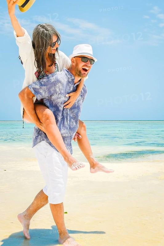 Carefree young man woman piggyback ride walking along turquoise ocean sand beach global tropical island resort destination sunny summer honeymoon getaway