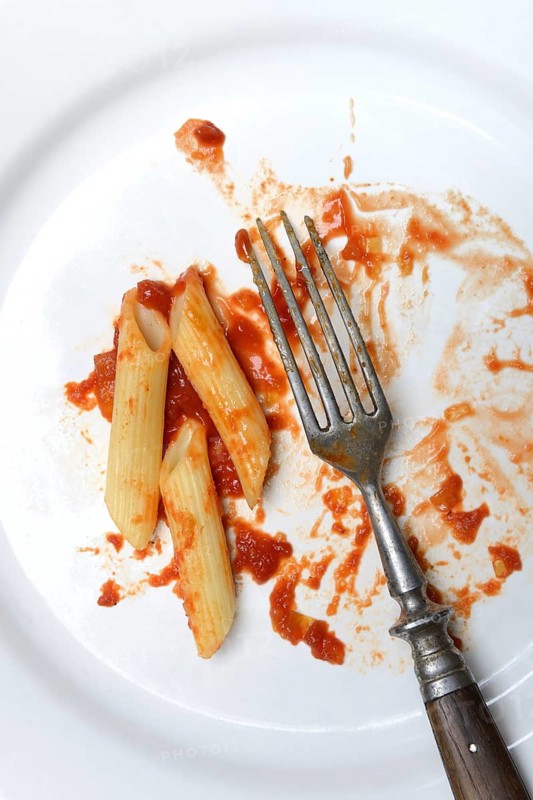 Plate with fork and leftover pasta, penne and tomato sauce, food waste