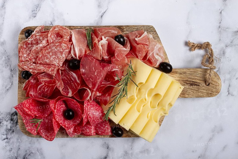 Assorted meat, appetizer, prosciutto, salami and ham, with maasdam cheese and olives, on a wooden board, breakfast, top view, close-up, no people