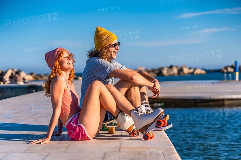 Young skaters laughing and enjoying a vibrant summer sunset by the sea, sharing joyful moments together on the pier