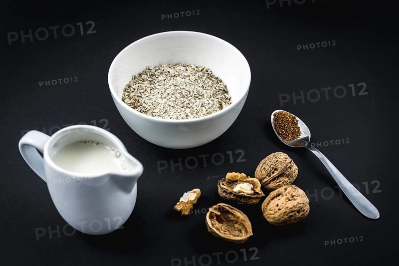 Oatmeal in a cup and winged walnuts and sugar black background. Oatmeal recipe with walnuts, prunes, cinnamon and sugar