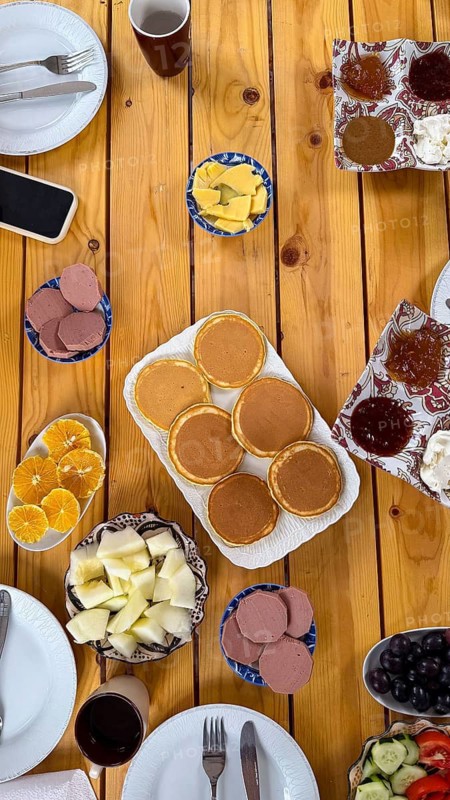 Wooden table filled with a diverse and healthy morning meal. Featuring golden pancakes. An assortment of fresh fruits. Jams. And other delicious components