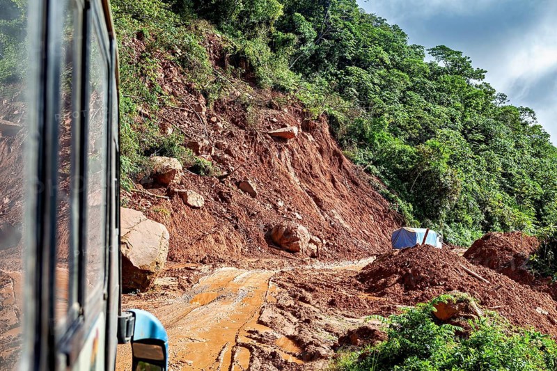 A landslide blocks the road, the bus navigates through the rough, red terrain, bus ride from La Paz towards Rurrenabaque through the rainforest on the Road of Death in Bolivia