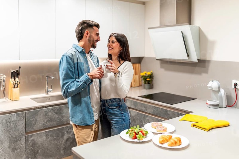 Young couple embracing and drinking coffee in their modern kitchen, with breakfast pastries and fresh fruit on the counter