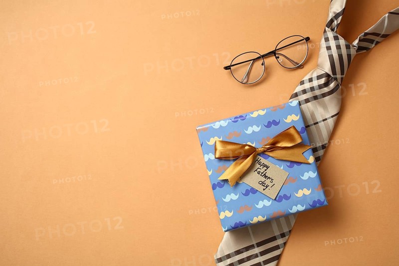 From above, a well wrapped Father's Day gift with a tie and glasses craftily arranged on a orange backdrop, emphasizing themes of love, appreciation, and celebration