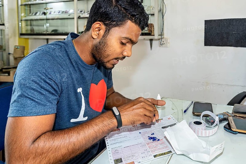 Man working concentrated at a table with documents and small stones surrounded by office supplies, The gemstone cutters in the city of Ratnapura in Sri Lanka