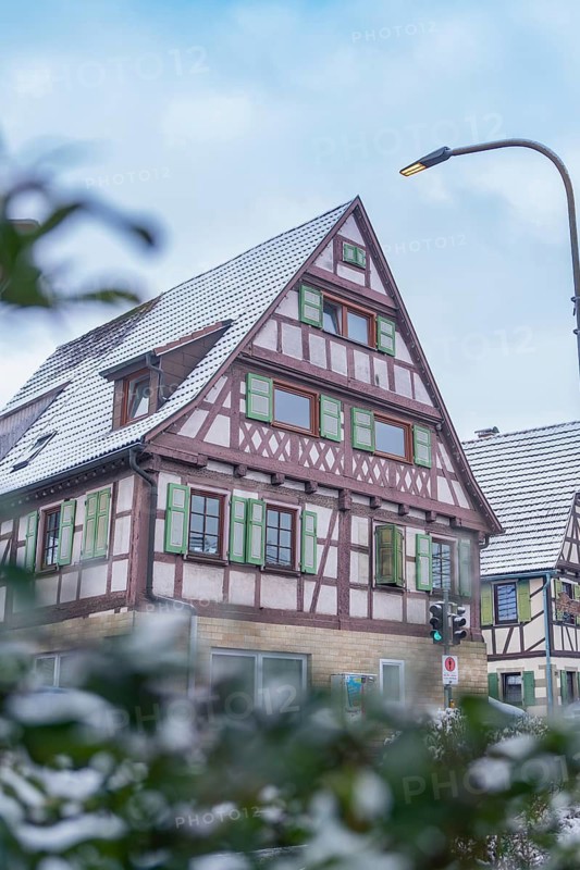 Snow-covered half-timbered house in a quiet street, surrounded by a few bushes and a lantern, Aidlingen, Böblingen district, Germany