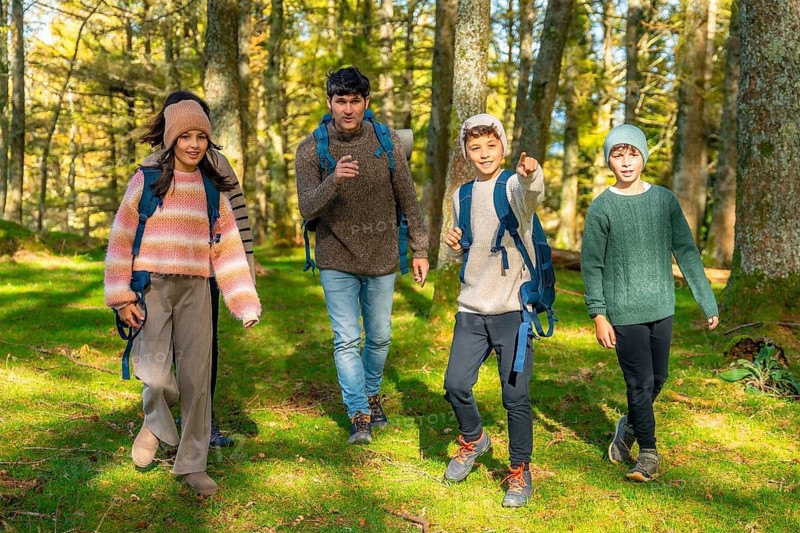 Teenage boy pointing ahead while trekking with the family at forest in a sunny day of autumn