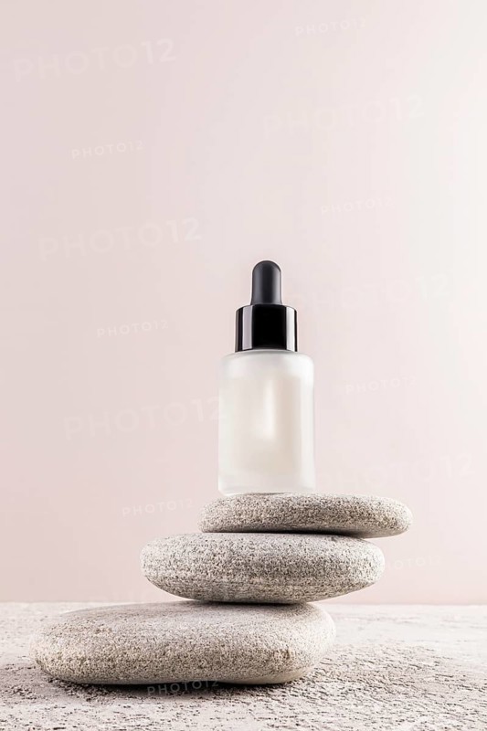 A minimalist image featuring a serum bottle with a black dropper, elegantly balanced on smooth stones The soft background highlights simplicity and modern beauty