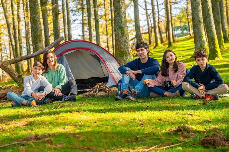 Portrait of a family sitting next to camping tent and bonfire enjoying nature together