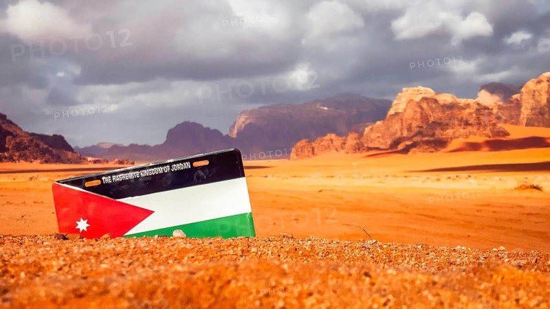 Wadi Rum red sand desert with Jordan flag installation dramatic sandstone mountains colorful sunset clouds iconic Middle East scenery
