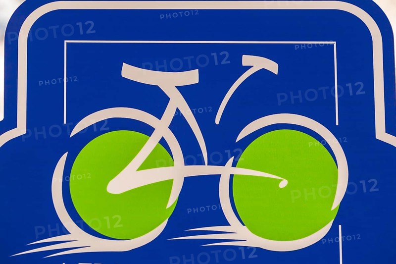 Close-up of speeding white bicycle with big bright fluorescent lime green wheels illustration on blue metal pictogram sign on bicycle route, Quebec, Canada