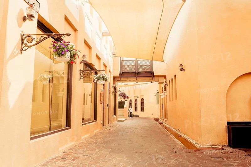 Doha, Qatar - 8th january, 2026: Narrow stone street Katara Cultural Village Doha. Traditional sand-colored buildings, hanging flower baskets, vintage wall lamps. Exterior architecture detail concept