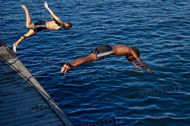 Zwei Jungen springen synchron ins blaue Wasser bei hellem Sonnenschein, Kopenhagen