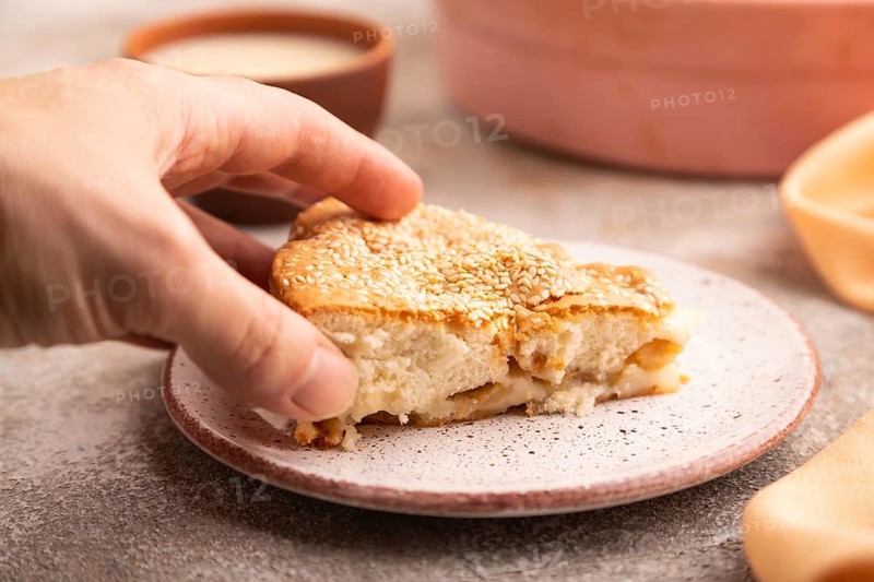 Apple Charlotte cake with hand on brown concrete background and orange linen textile, cup of milk, side view, close up, selective focus