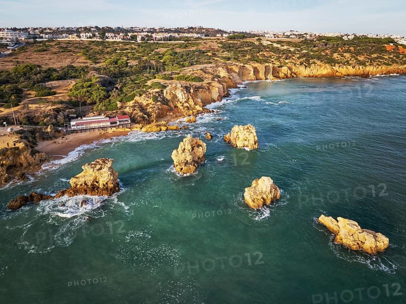 Aerial view of Praia dos Arrifes shoreline with sea stacks, cliff paths, beach access and waves around the rocks