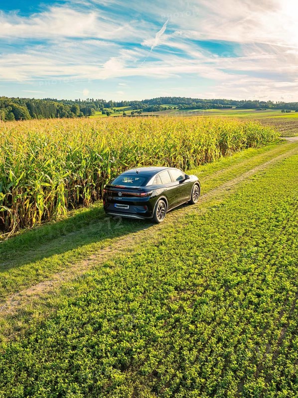 Black car driving on a dirt road next to a corn field under a blue sky with white clouds, Carsharing, VW ID5, Calw, Black Forest, Germany