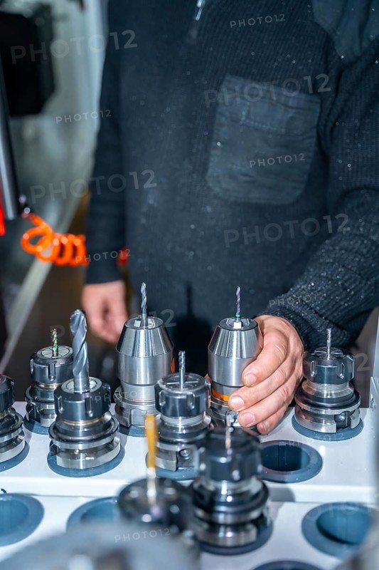 Vertical photo of an unrecognizable worker holding one lathe among a collection of lathes in a cnc factory
