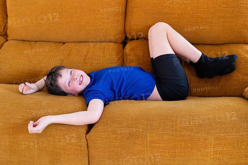 A young Caucasian boy joyfully lying on an orange sofa at home, showcasing his missing milk teeth with a broad smile, indicating a childhood milestone