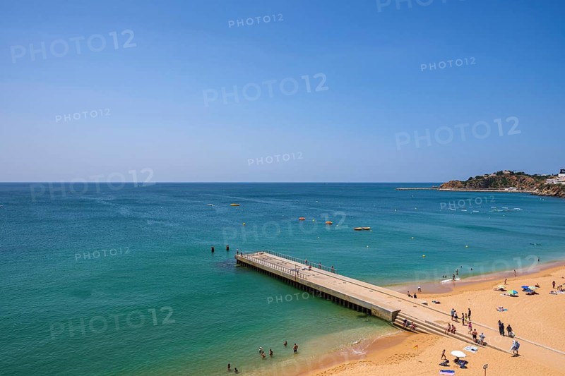 A sunny beach with crystal clear water, a jetty and people relaxing on the beach, Albufeira, Faro, Portugal