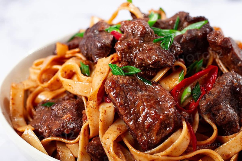 Udon noodles with Mongolian beef, green onions and vegetables, in a white plate, on a light background, homemade, no people