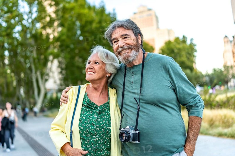 Happy elder woman embraced to man with photographic camera in a park