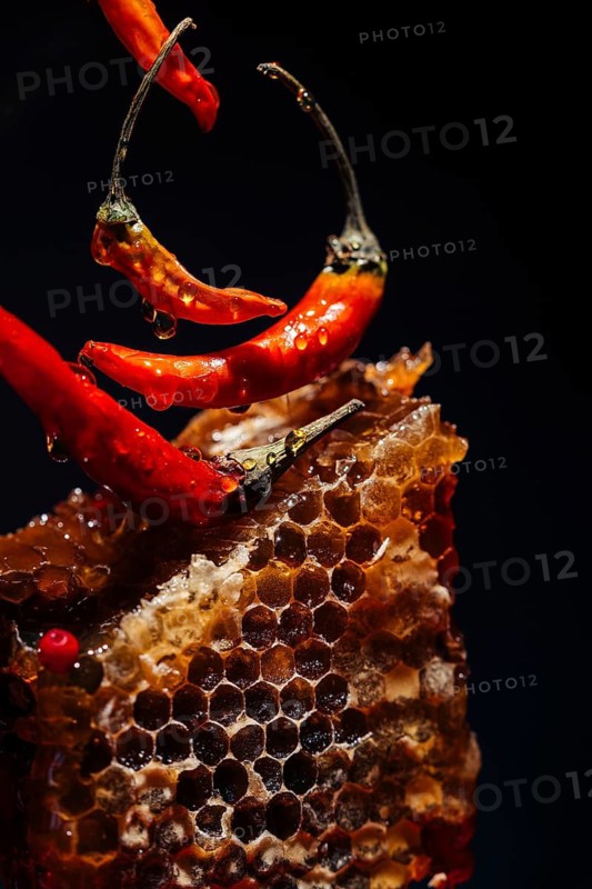 Close up of vibrant red chilies and a honeycomb against a dark background. Droplets add texture and allure, highlighting the contrast between spice and sweetness