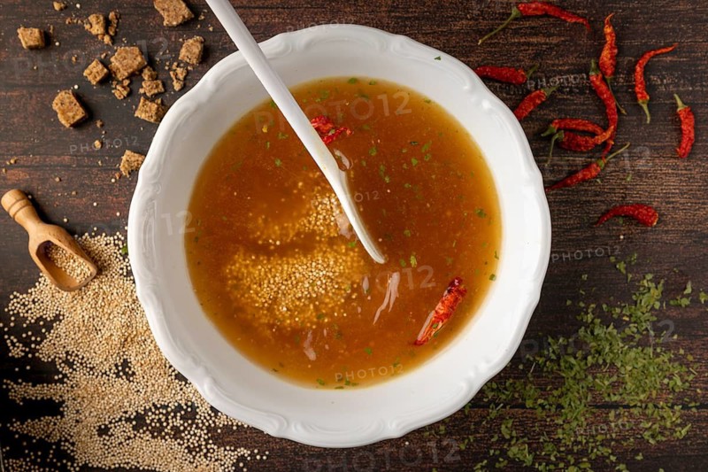 Broth with quinoa, parsley and red hot peppers in a bowl, surrounded by ingredients
