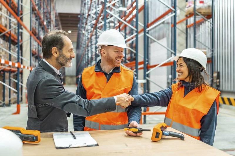 Manager and warehouse workers engaging in a handshake after successfully closing a deal within a bustling logistics center