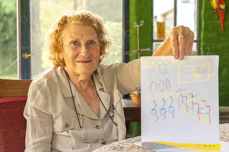 Happy grandmother proudly displaying a colorful drawing made by her grandchild, enjoying a heartwarming moment of connection and creativity in a cozy home setting