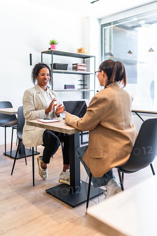 Two businesswomen are having a productive meeting, discussing a project over a laptop in a bright, modern cafe
