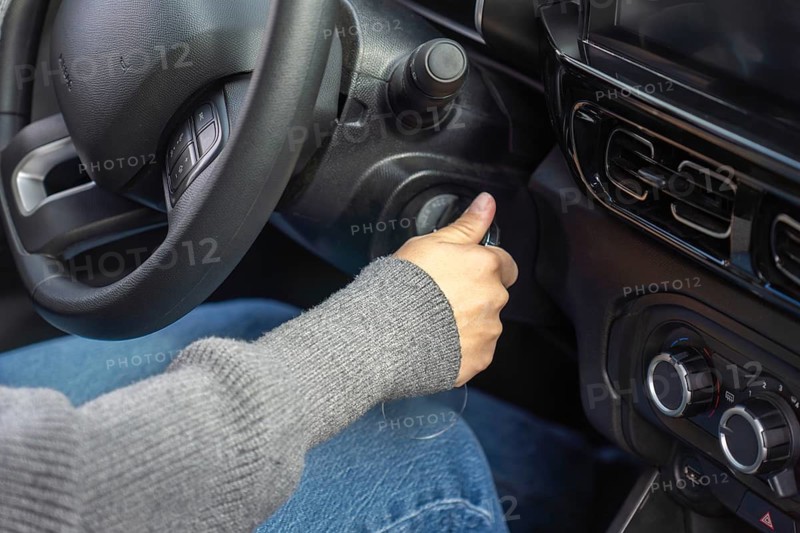 Close-up of student driver's hand approaching the ignition switch, steering wheel and dashboard visible, car interior, driving lesson concept