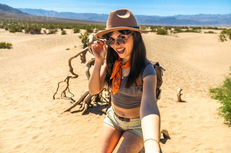 Woman traveler exploring the arid death valley national park desert, holding her arm out for a selfie and smiling, enjoying the hot climate and adventure