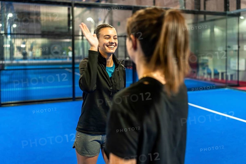 Two female padel teammates high fiving on a blue court, celebrating a win with smiles and energy teamwork, friendship, fitness and joyful post match bonding