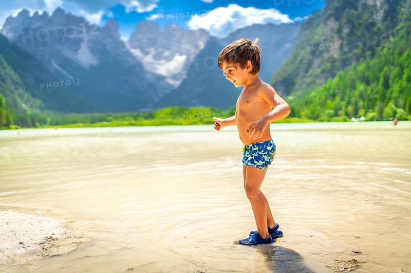 Happy child playing in the shallow waters of lake landro, enjoying summer fun against the stunning dolomites in italy