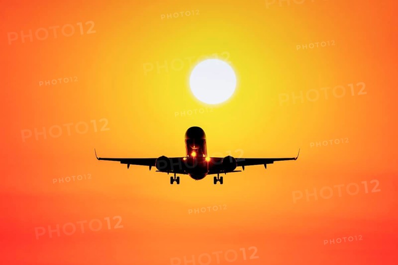 Airplane flying towards sunset in orange sky